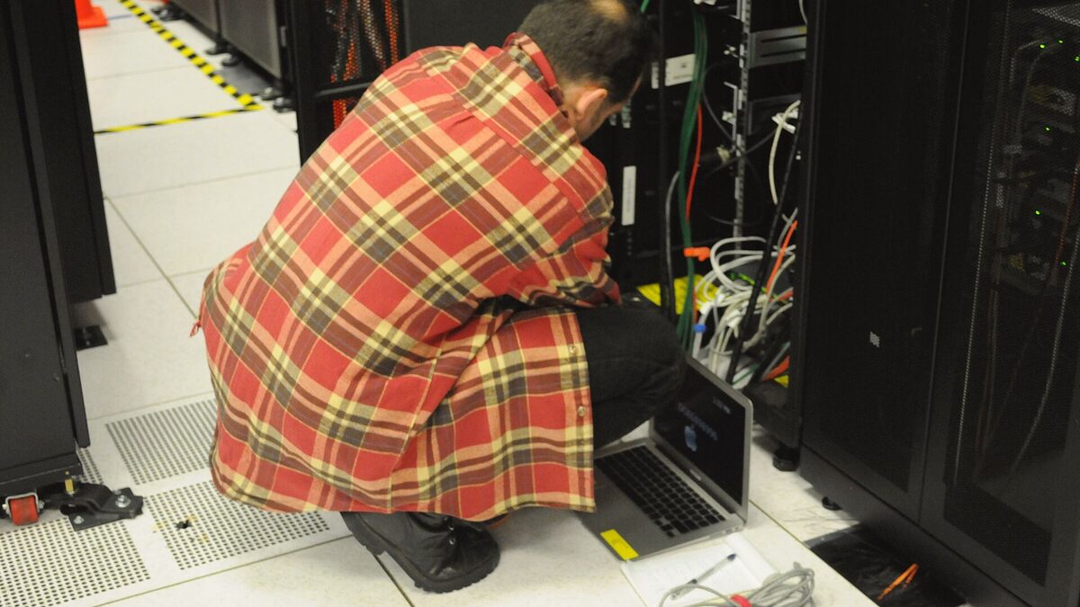 A technician at a server rack with a laptop, standing in for the SQL infrastructure Opexus ran for 45 federal agencies.