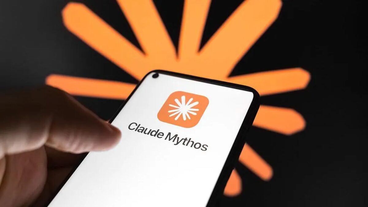 A hand holds a smartphone showing the Claude Mythos app logo against a dark backdrop with Anthropic's orange burst symbol.
