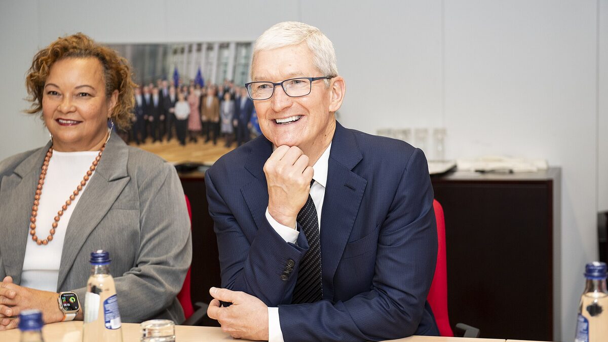 Tim Cook seated at a meeting table, smiling, during a visit to the European Commission