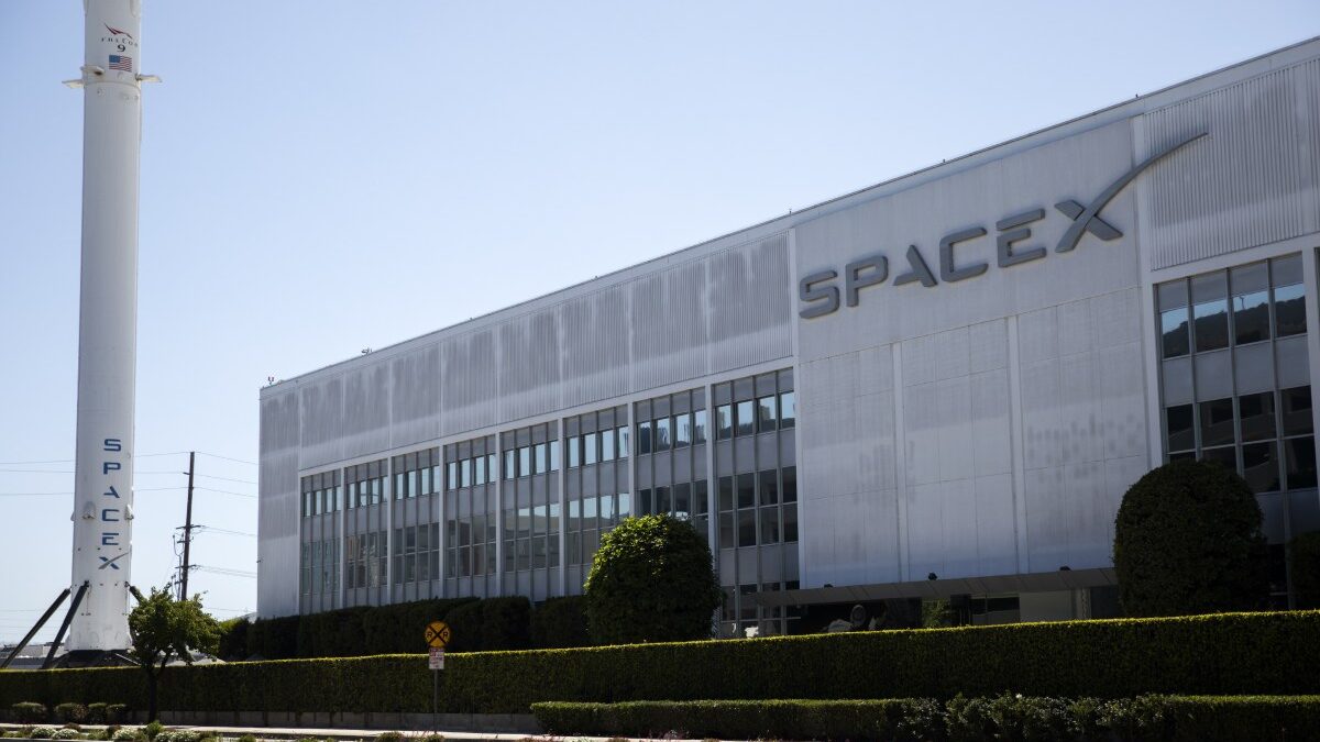 Elon Musk speaking at an event, with Tesla and SpaceX branding behind him